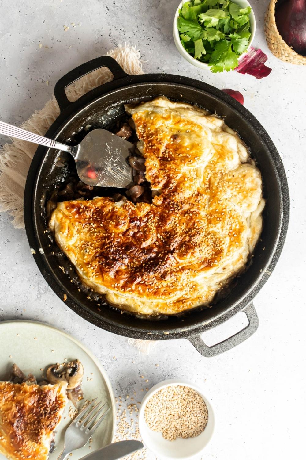 An overhead view of an iron cooking pan with cooked beef pot pie in it with a slice taken out of it. A spatula sits in the place where the slice was.