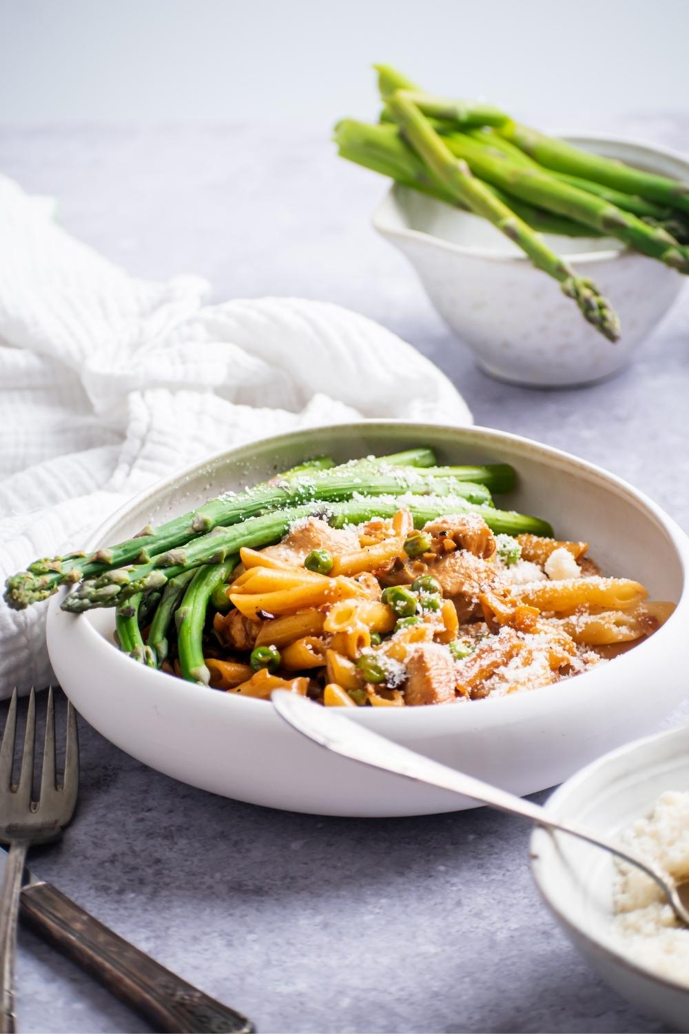 A bowl with Spicy Chicken Chipotle Pasta and asparagus topped with parmesan cheese.