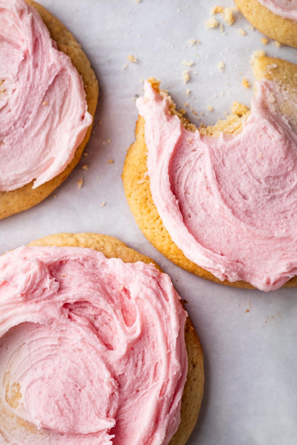 A close-up of three sugar cookies with pink icing on them. One cookie has a bite taken out of it.