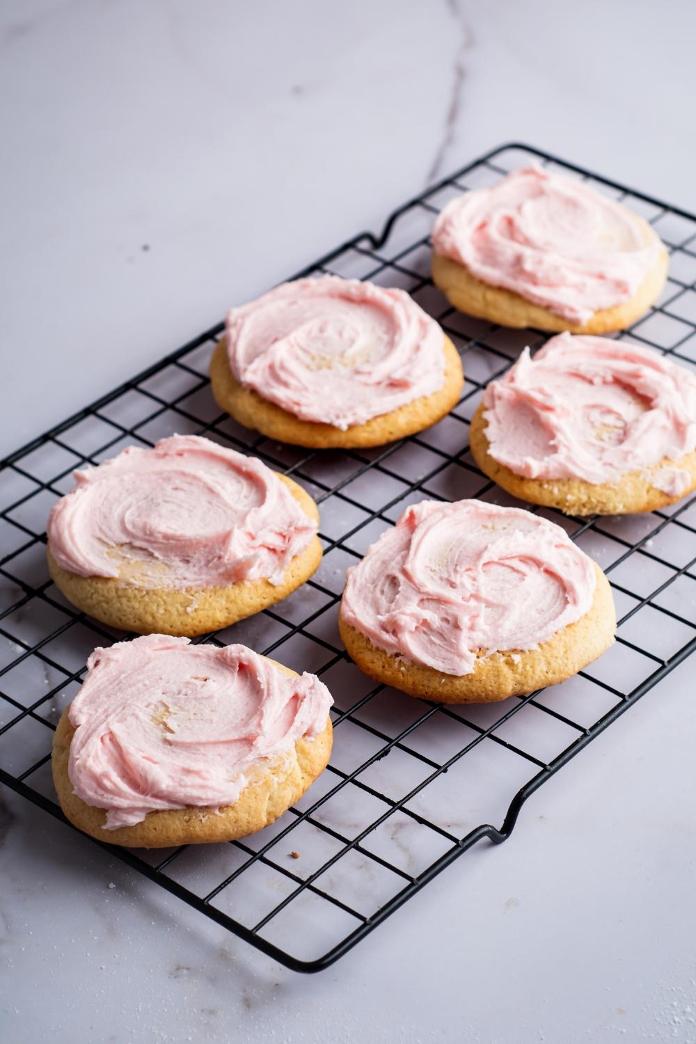 A cooling rack with six sugar cookies with pink icing on it.