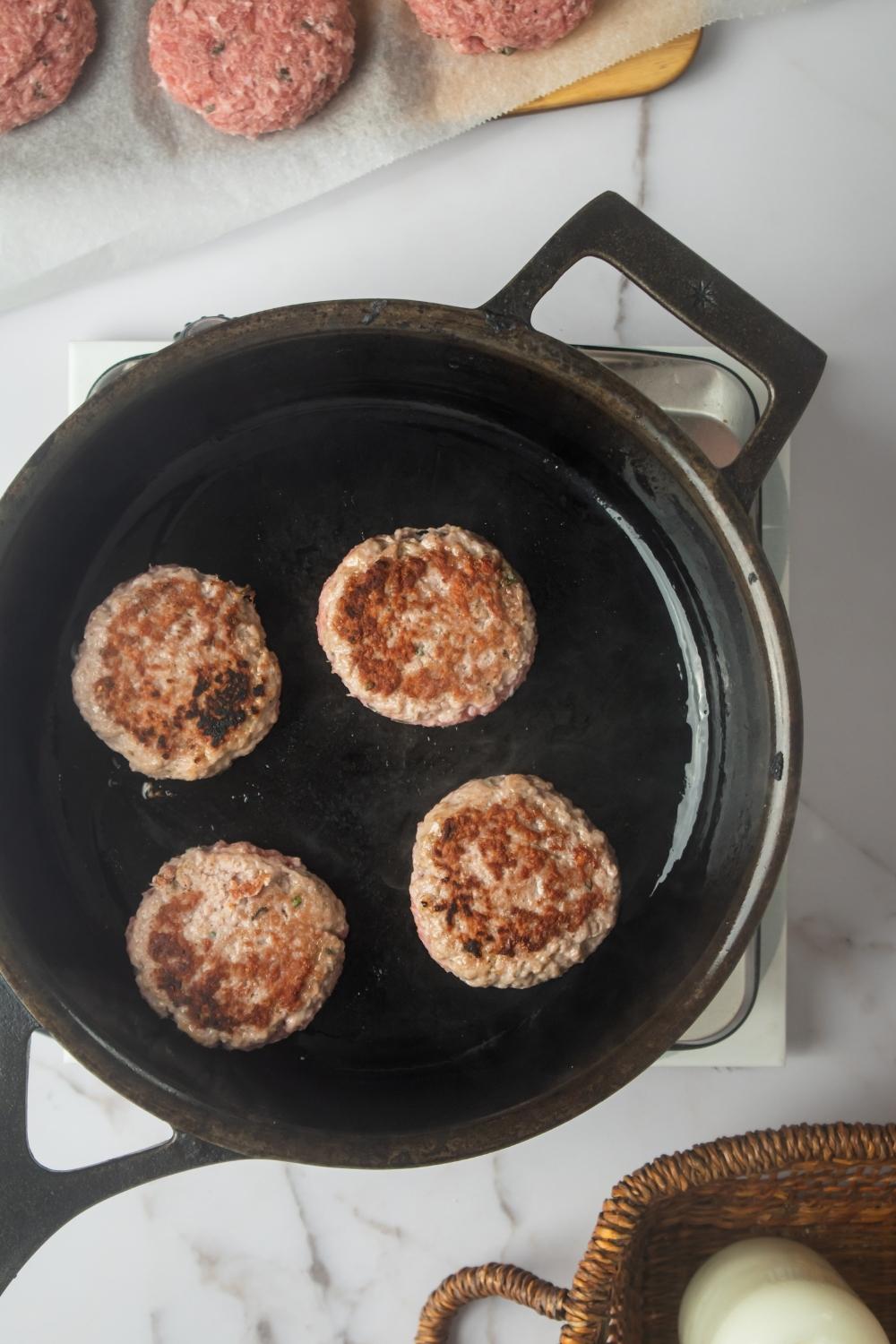 An overhead view of a skillet with four Jimmy Dean patties cooking on it.