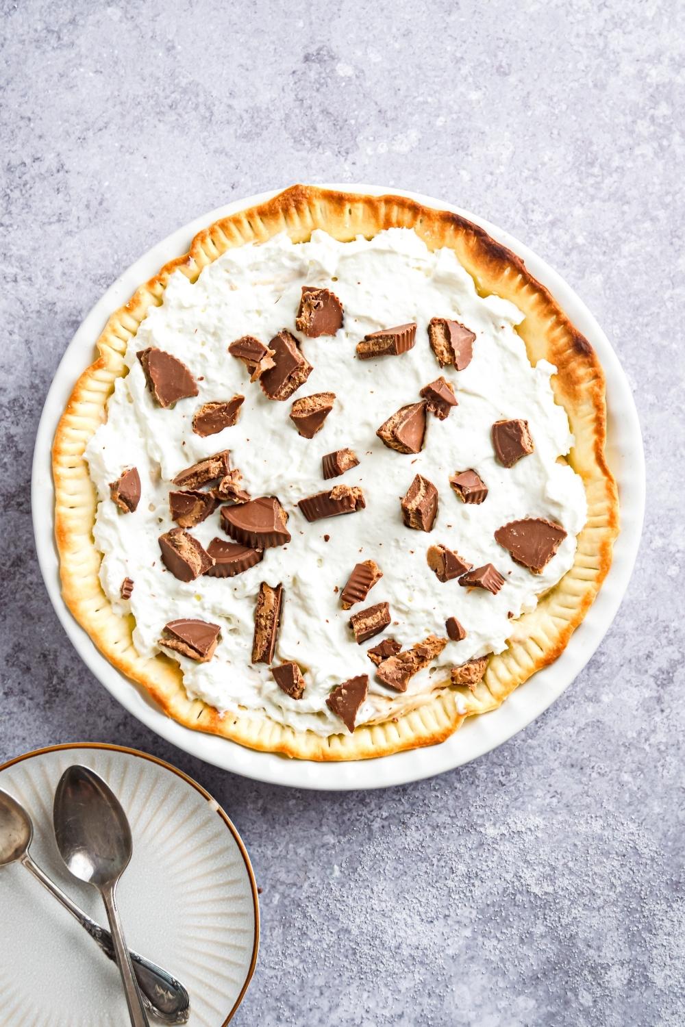 An overhead view of a Reeses pie topped with homemade whipped cream and chunks of Reese's peanut butter cups.