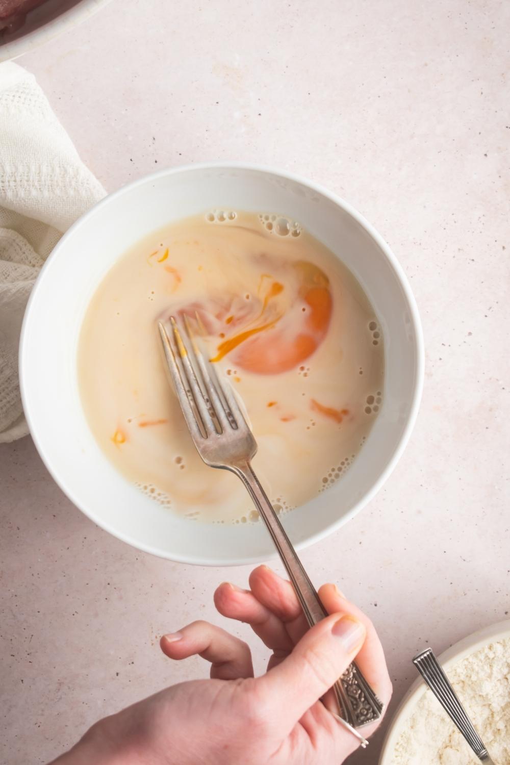 An overhead view of a bowl with the mar far chicken batter being mixed with a fork.