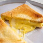 A close-up of a plate with an air fryer grilled cheese half with overflowing melted cheese down the side.