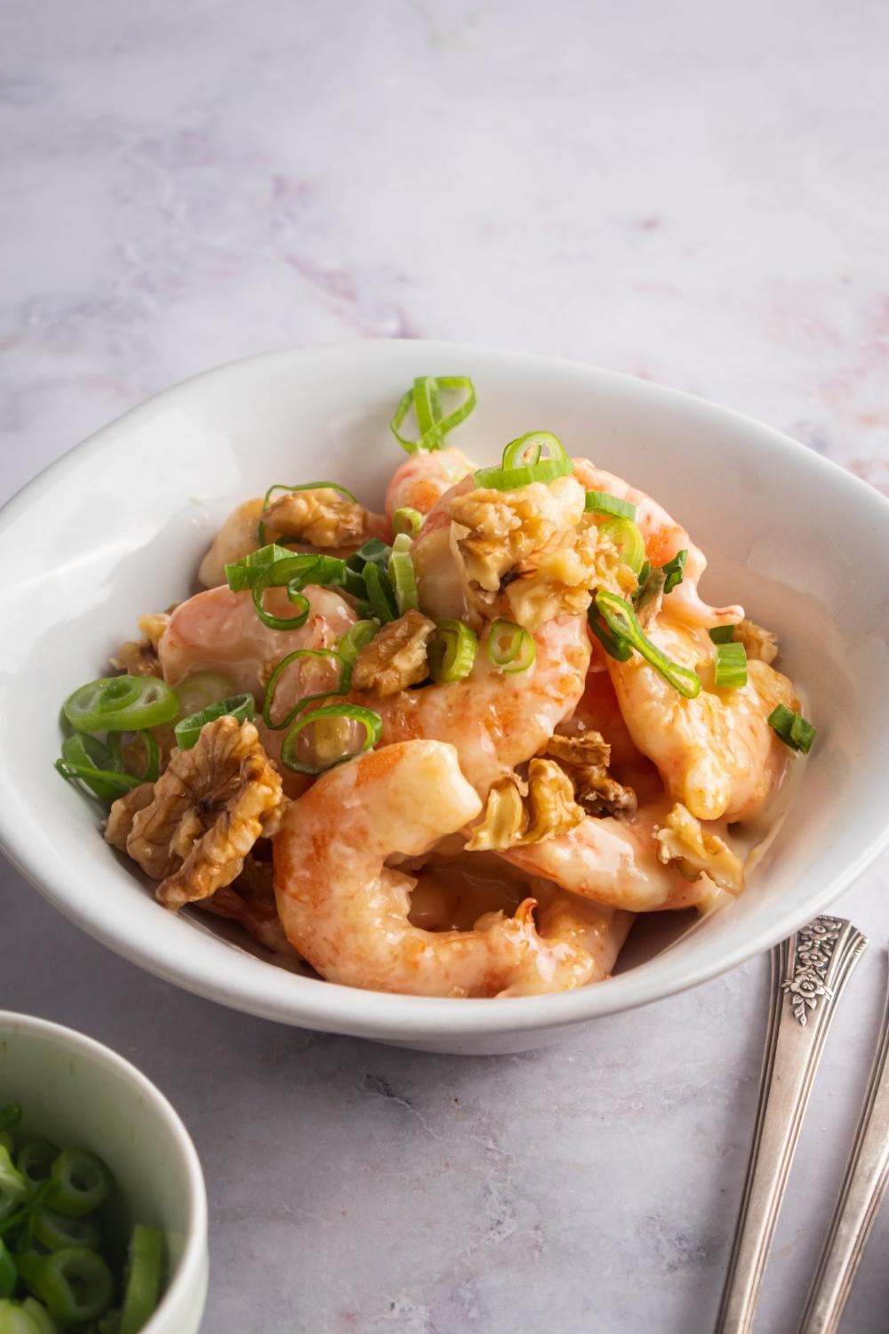 A bowl with panda express honey walnut shrimp topped with chopped green onions.