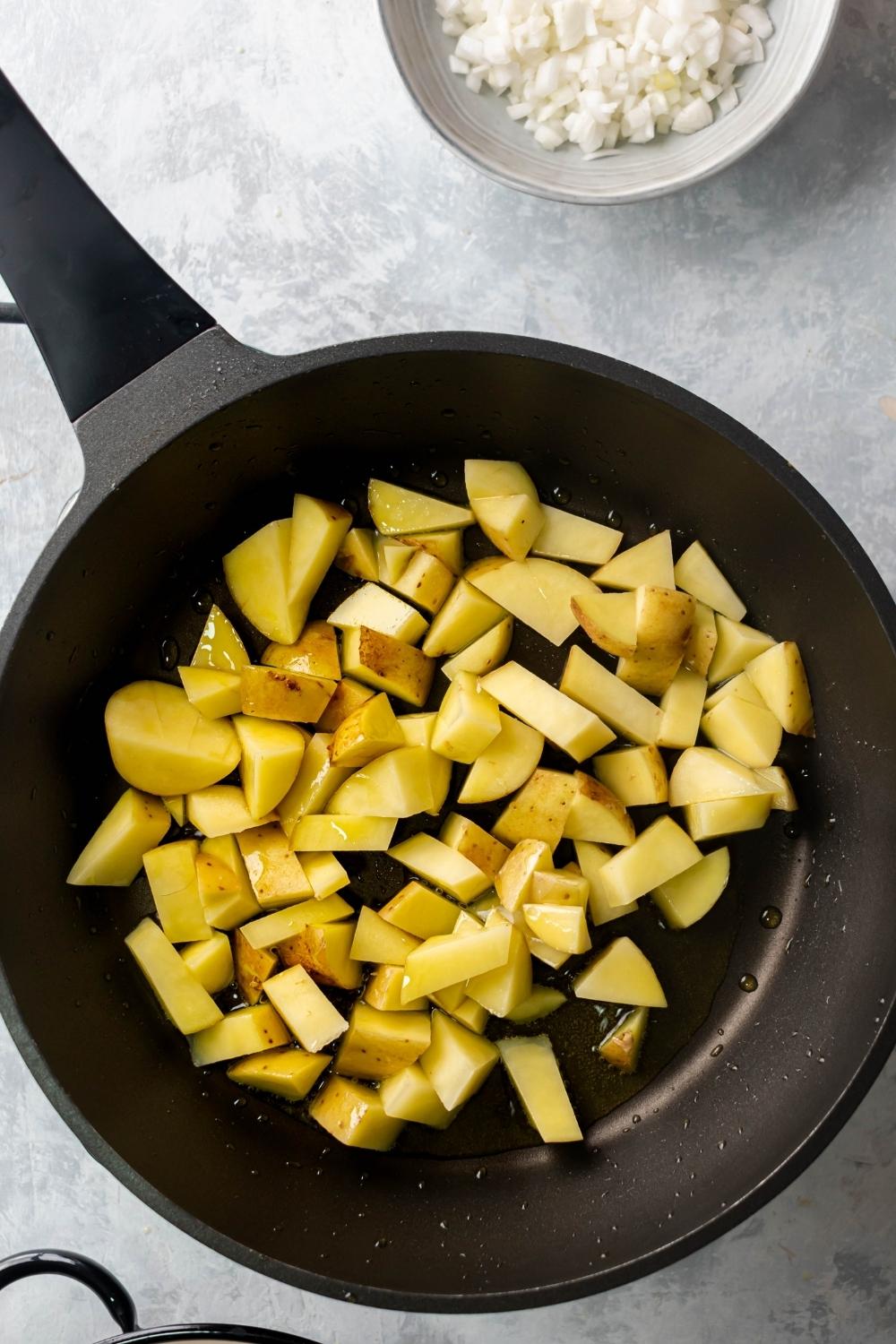 An overhead view of cubed potatoes in an iron pan with oil.