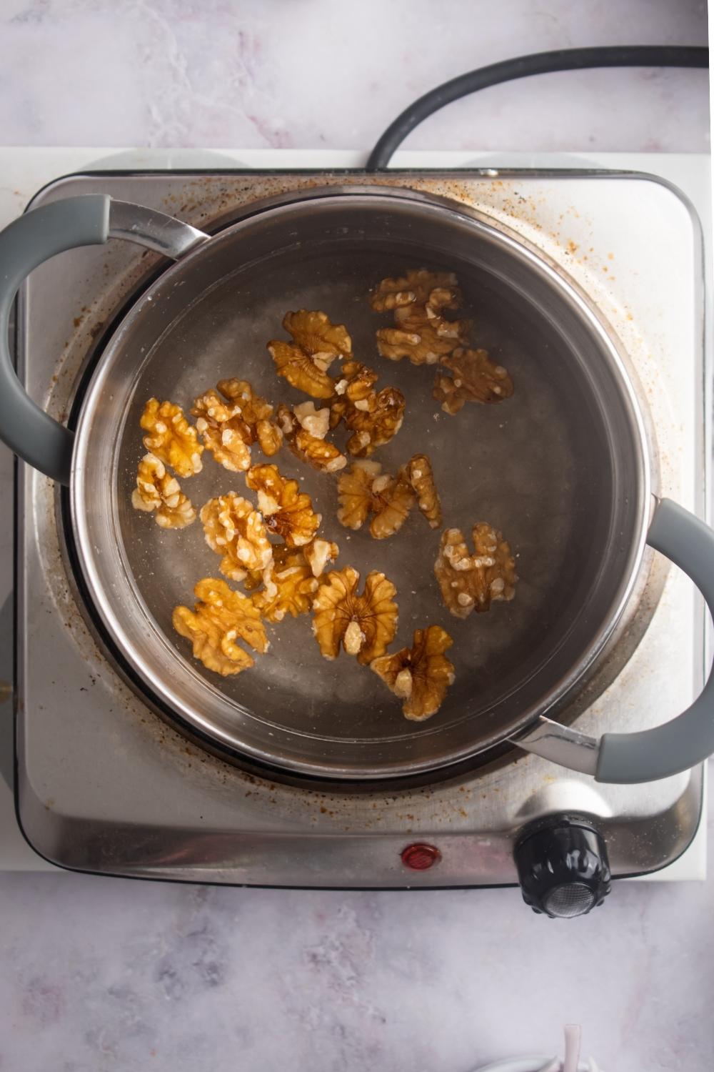 An overhead view of a pot with boiling water, sugar, and walnuts.