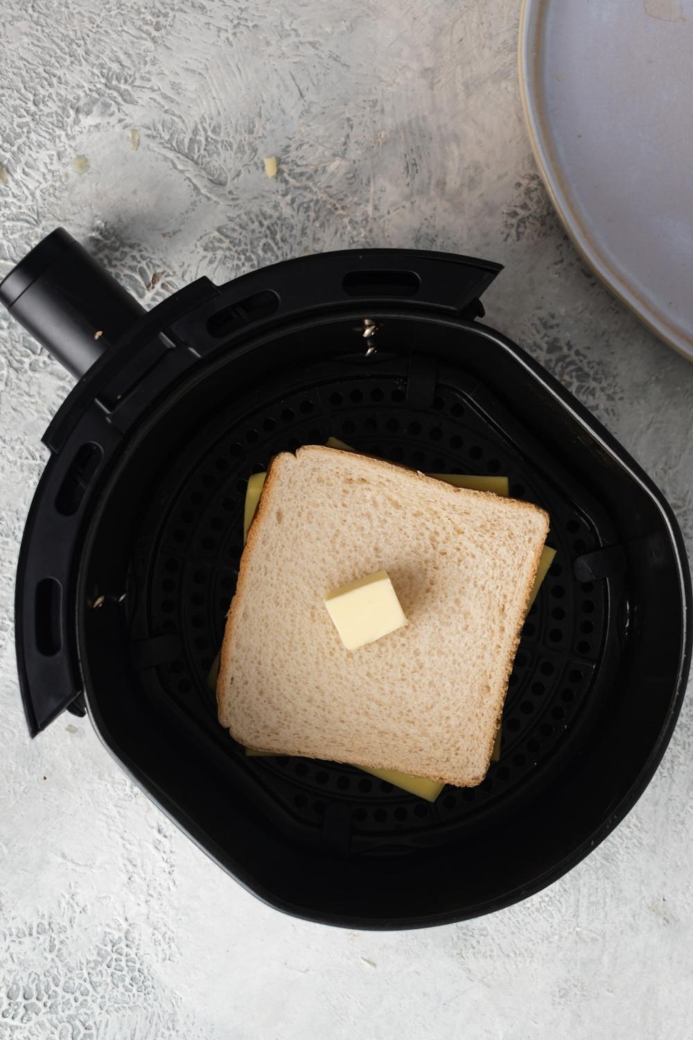 An overhead view of an air fryer with white bread buttered with cheese in the middle.