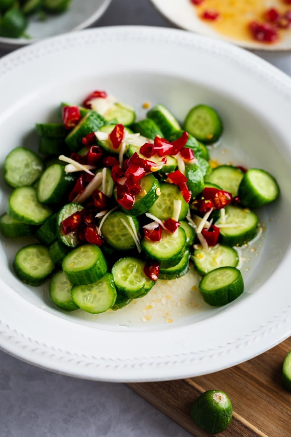 Red chilis on top of diced cucumbers in a white bowl.