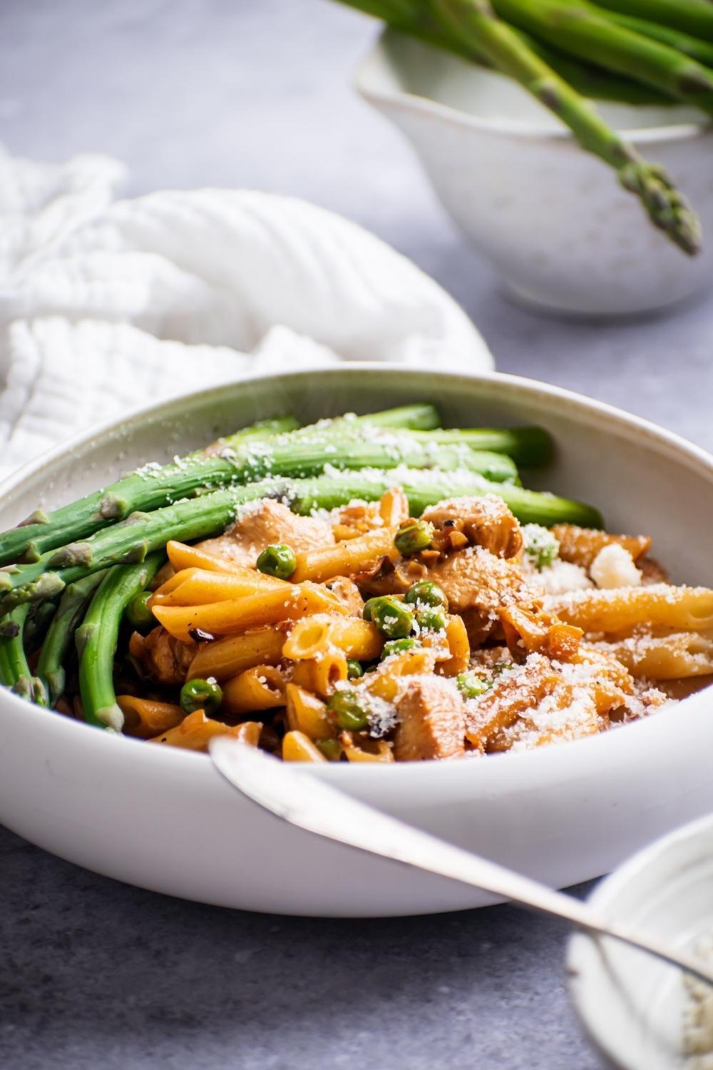 A side view of a bowl with Spicy Chicken Chipotle Pasta and asparagus topped with parmesan cheese.