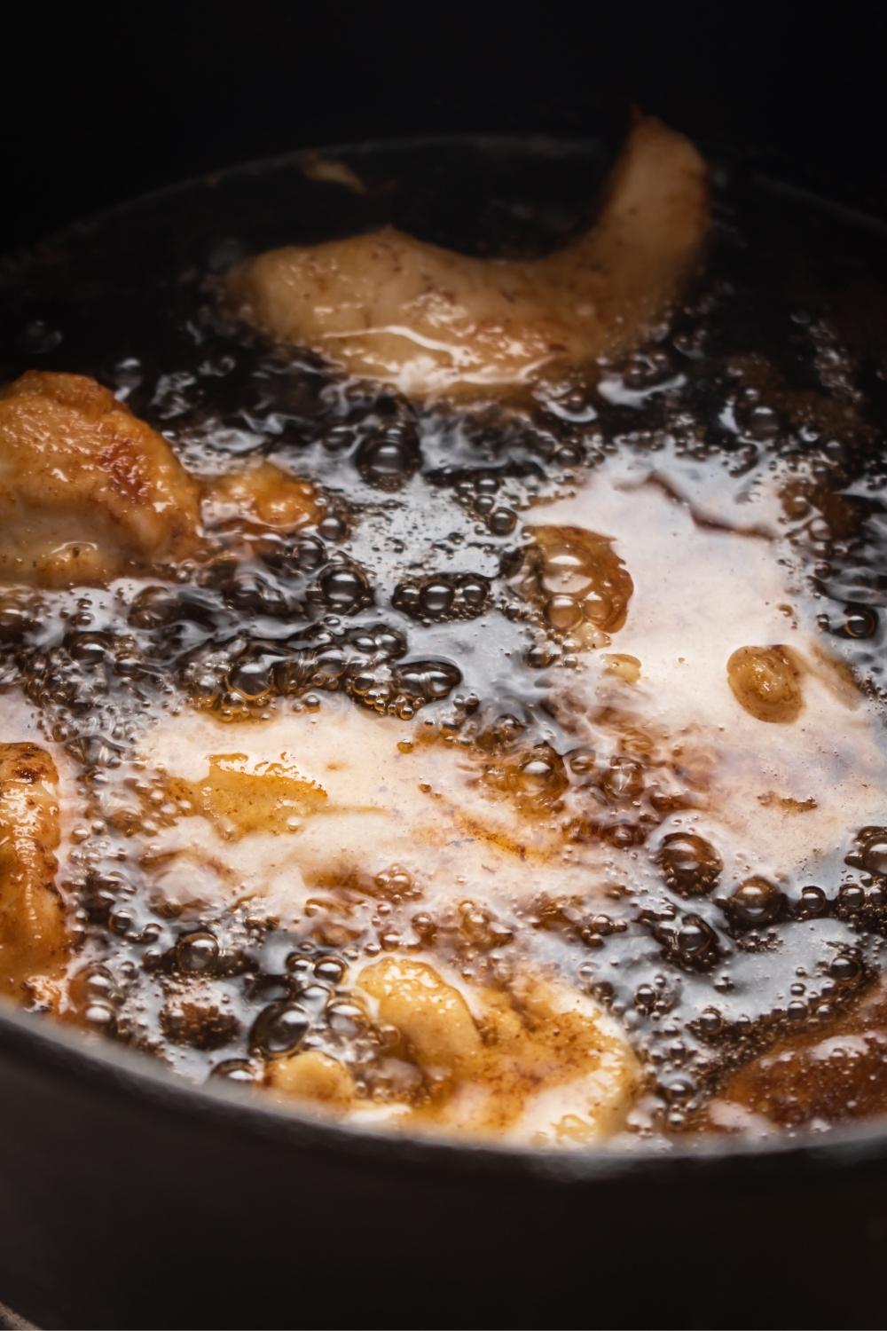 A close-up of a pan with hot, sizzling oil cooking Mar Far chicken chunks.