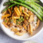 An overhead view of Spicy Chicken Chipotle Pasta with asparagus served on the side and parmesan sprinkled on top.