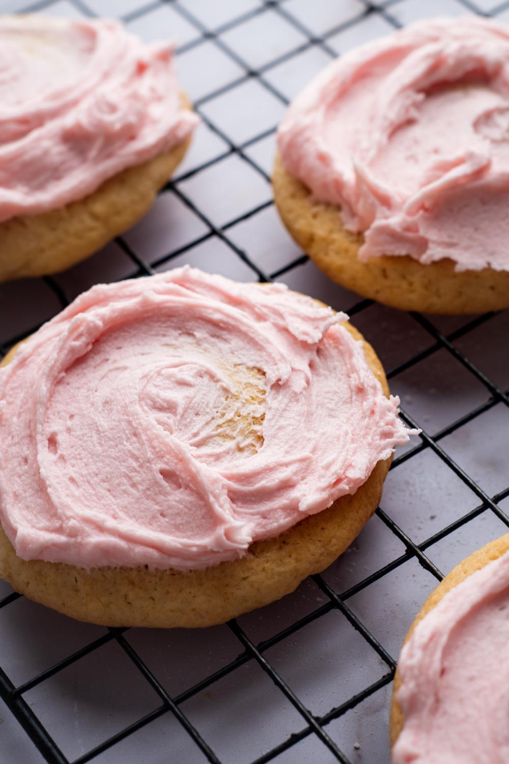 A close-up of for sugar cookies with pink icing sitting on a cooling rack..