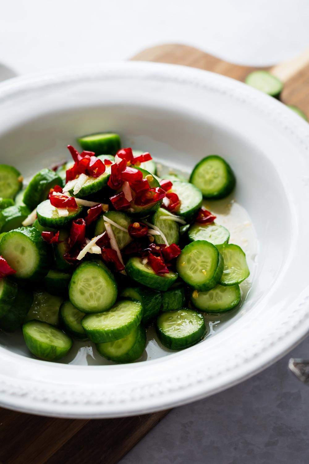 Part of a white bowl with red chilis and diced cucumbers in it.