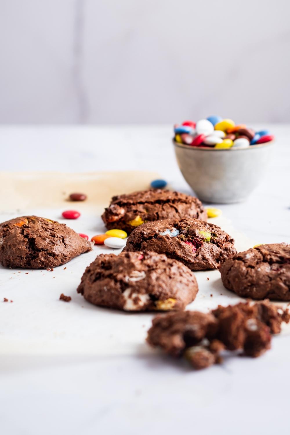 Five chocolate cake mix cookies in front of a bowl of m&ms.