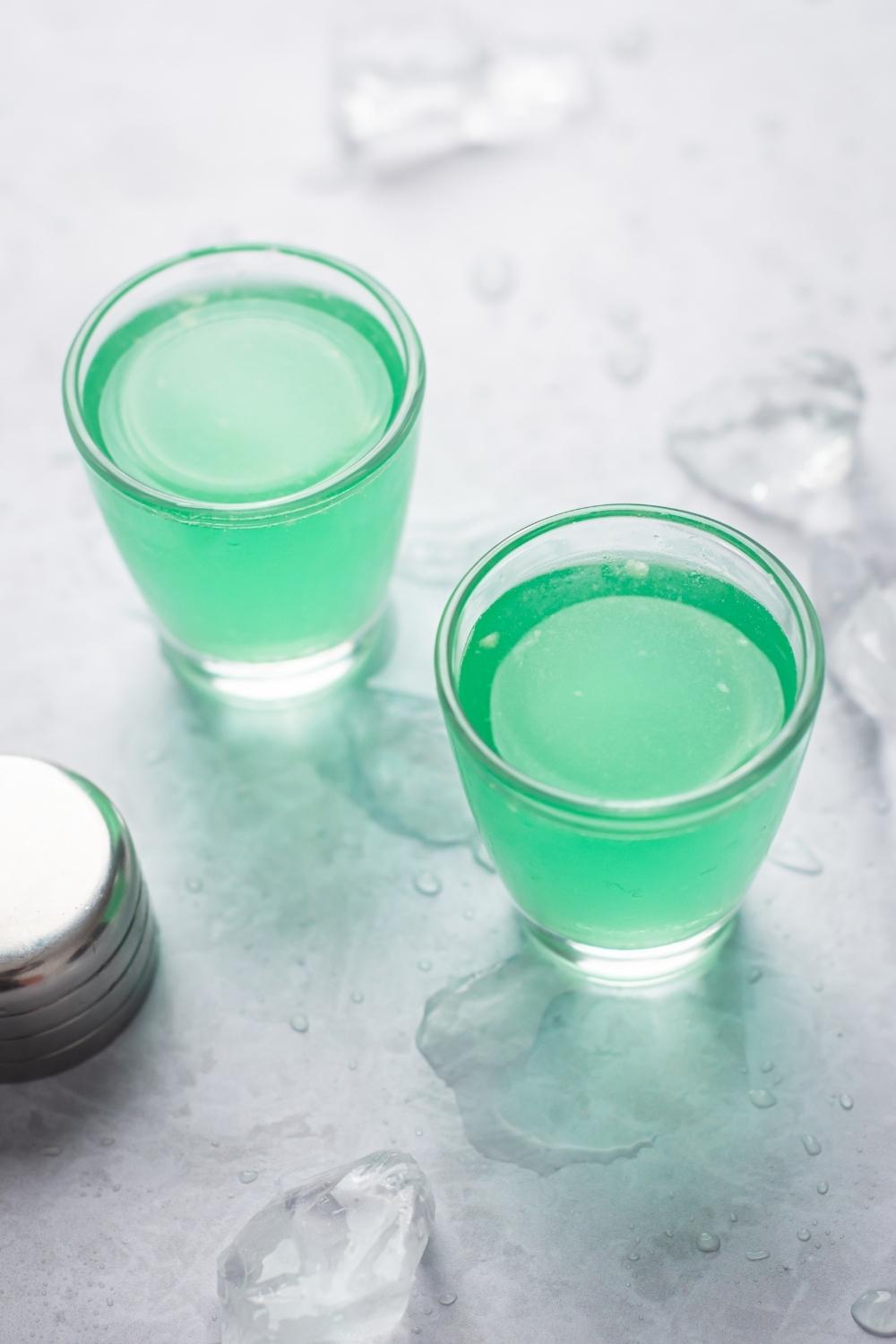 An overhead view of two marijuana shots in shot glasses. Ice is on the countertop surrounding the glasses.