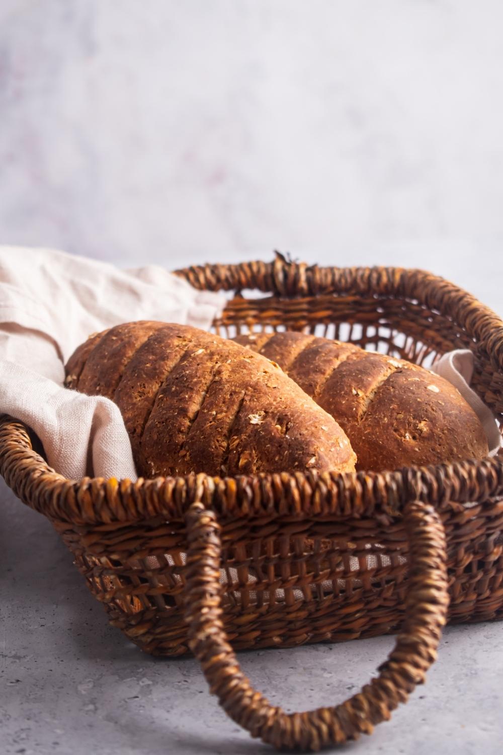 A side angle of two loaves of bread sitting in a basket lined with a kitchen towel.