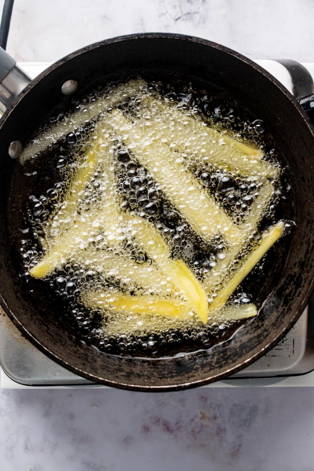 An overhead view of a pot with hot oil and fries frying.
