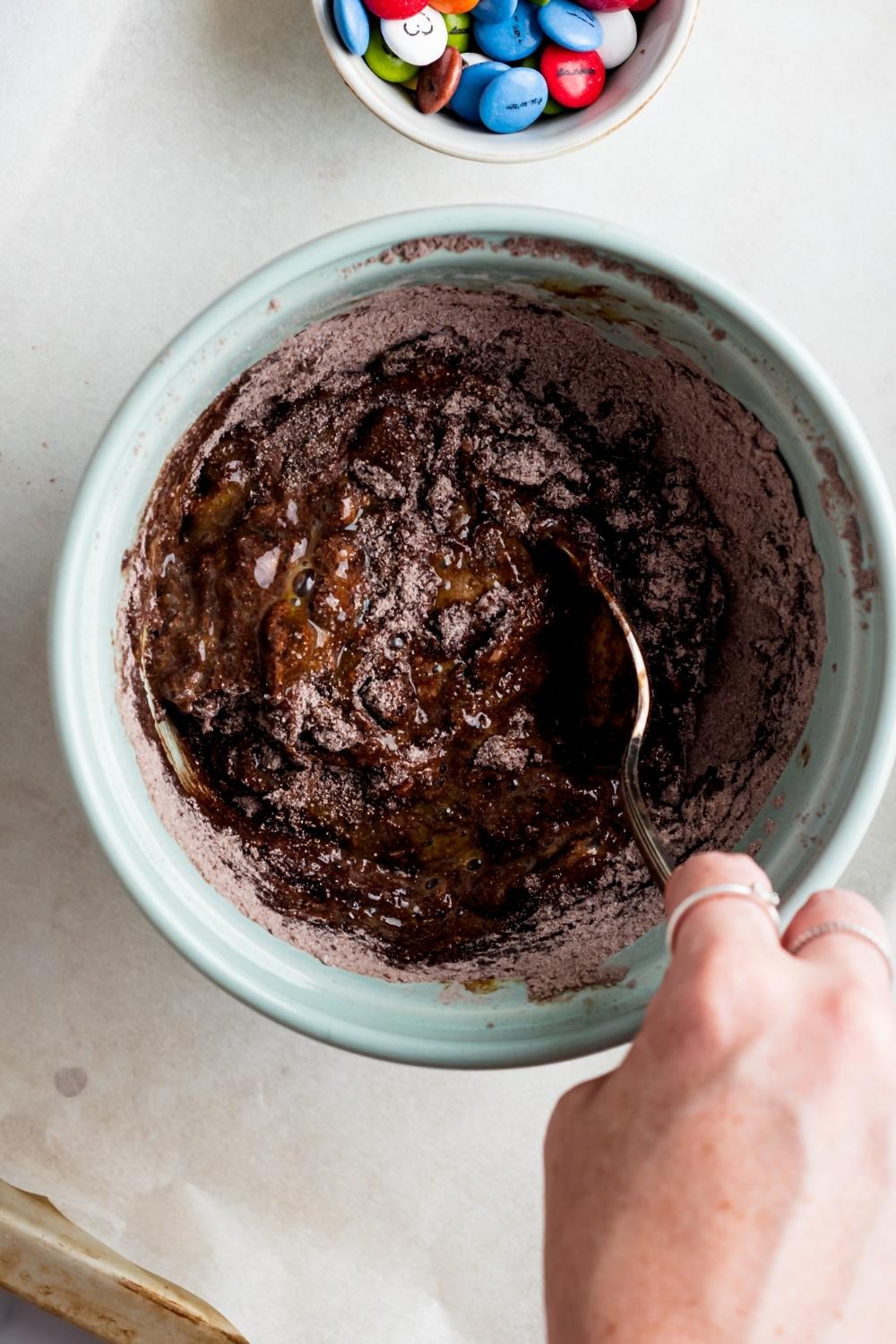 A hand mixing chocolate cake mix in a bowl with a spoon.