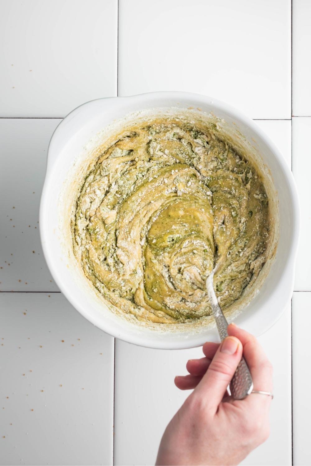 A hand mixing matcha brownie ingredients together.