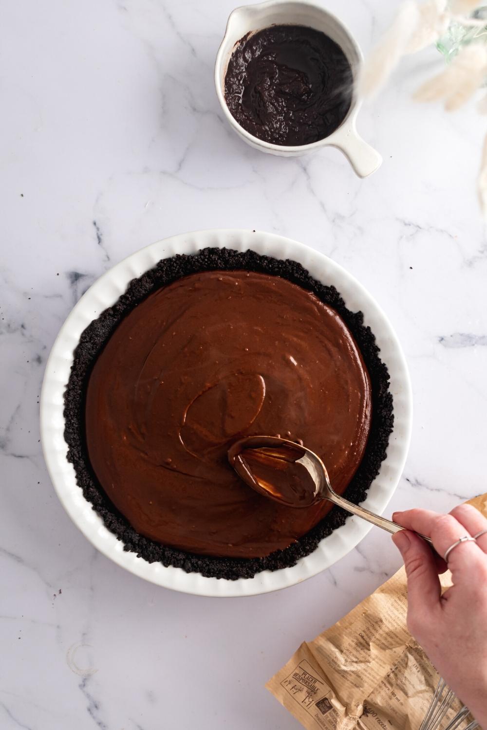 A hand spooning chocolate filling onto an Oreo pie crust.