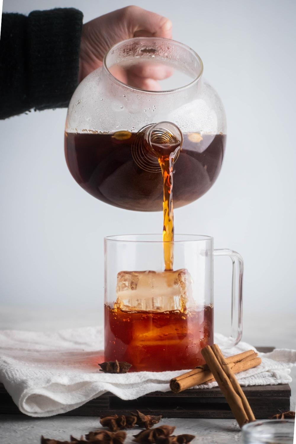 A hand pouring black tea into a glass cup filled with iced.