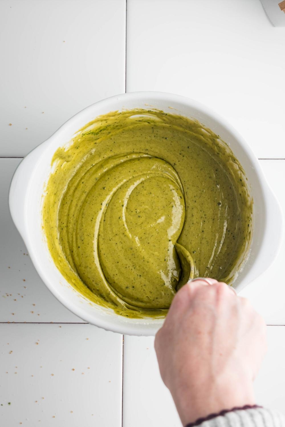 A hand mixing matcha brownie batter in a bowl.