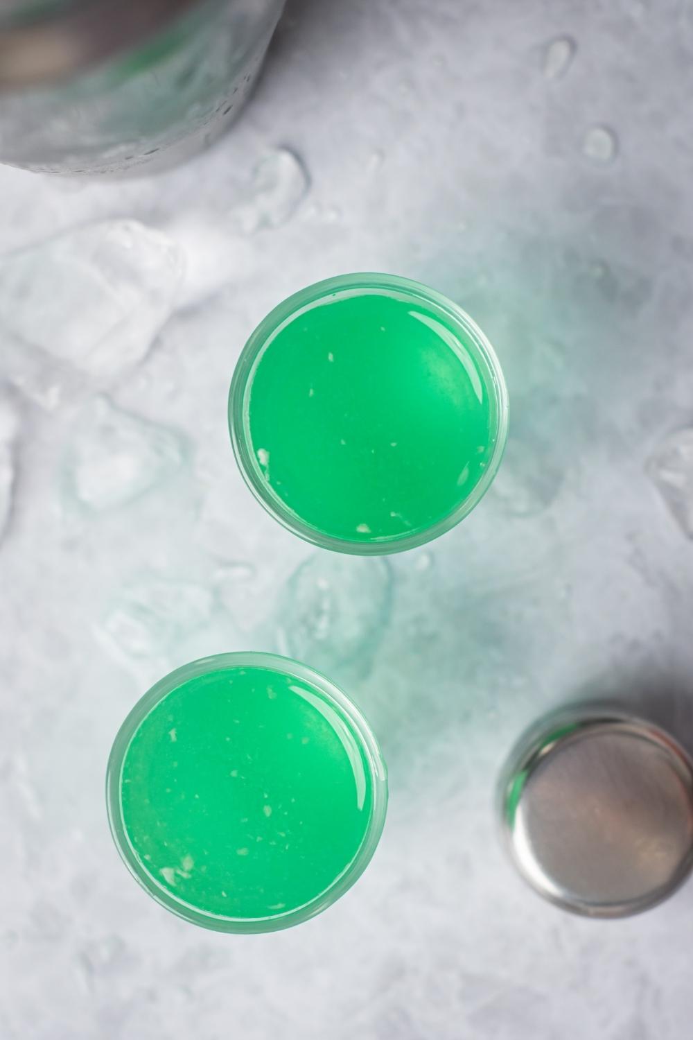 An overhead view of two marijuana shots in shot glasses. Ice is on the countertop surrounding the glasses.