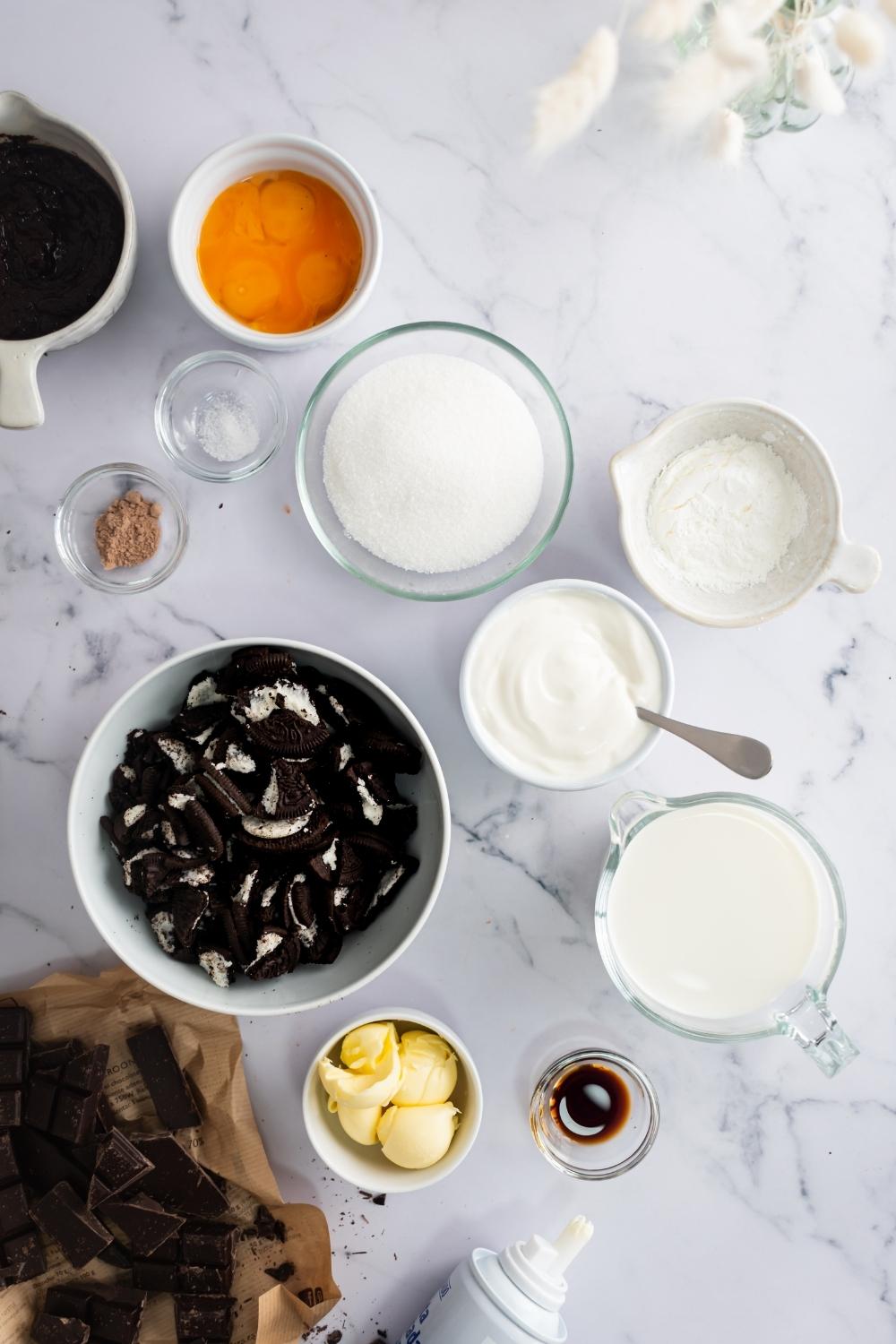 A bowl of oreos, a bowl of sugar, a bowl of butter, a bowl of cream, a bowl of espresso powder, and a bowl of eggs all on a white plate.