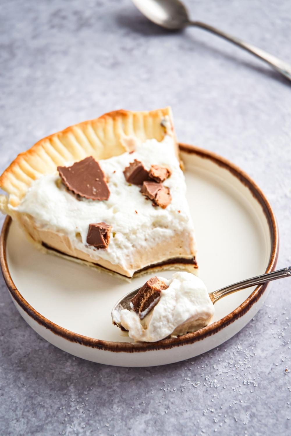 One slice of Reese's peanut butter pie on a small plate. A scoop is removed from the slice and on top of a spoon laying next to the pie slice.