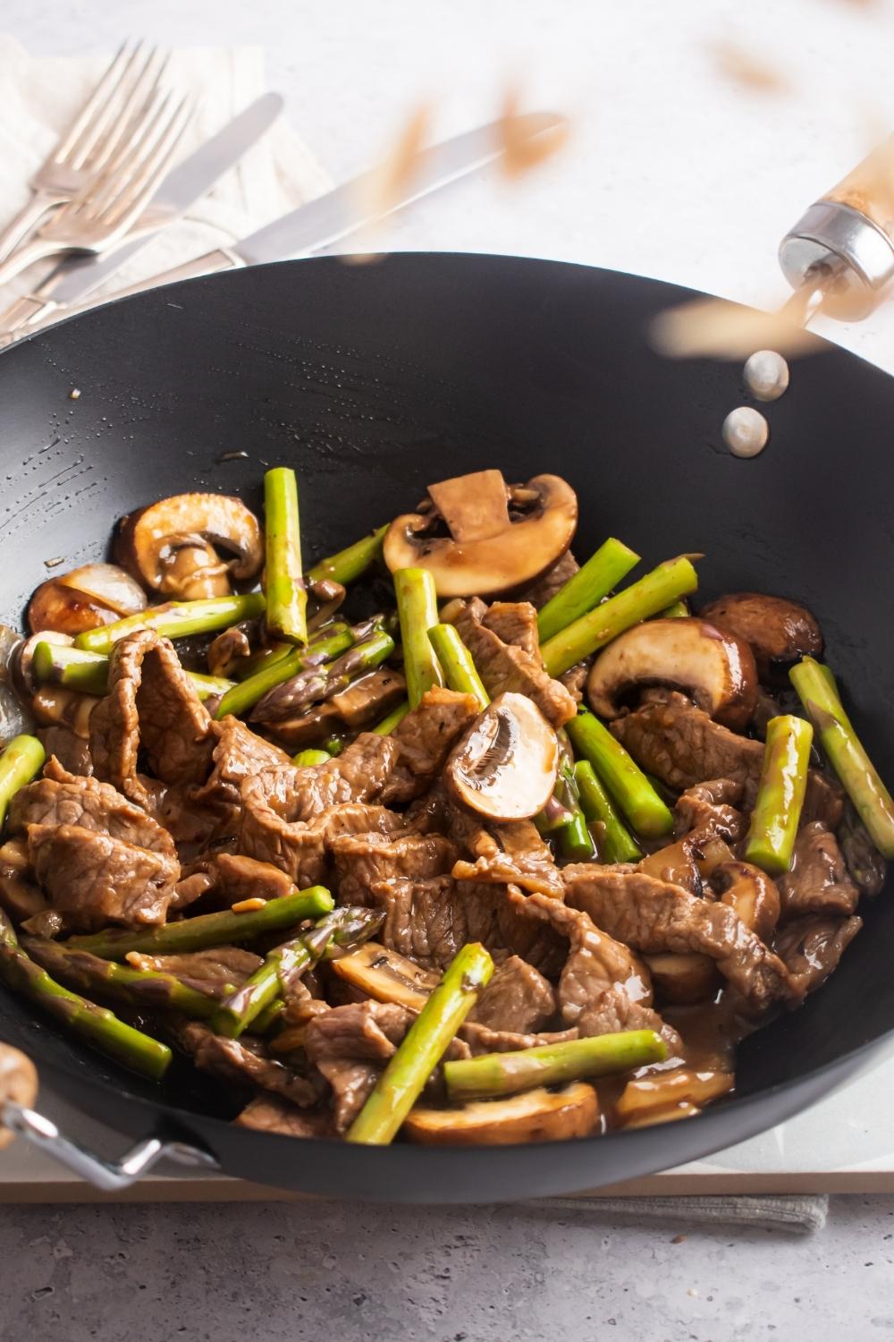 A wok filled angus steak, mushrooms, and asparagus.