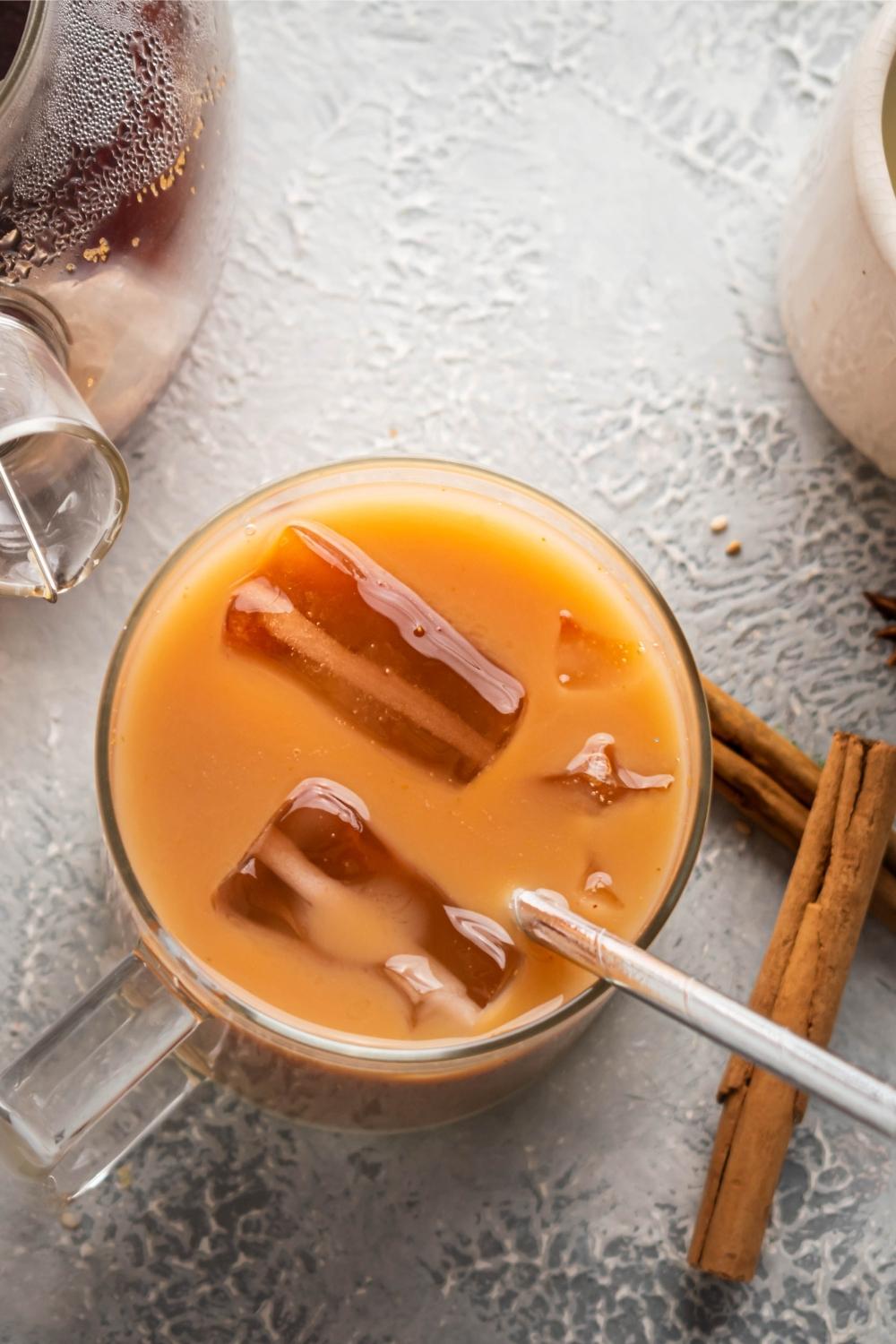 A glass of thai tea with some ice cubes and a straw in it.