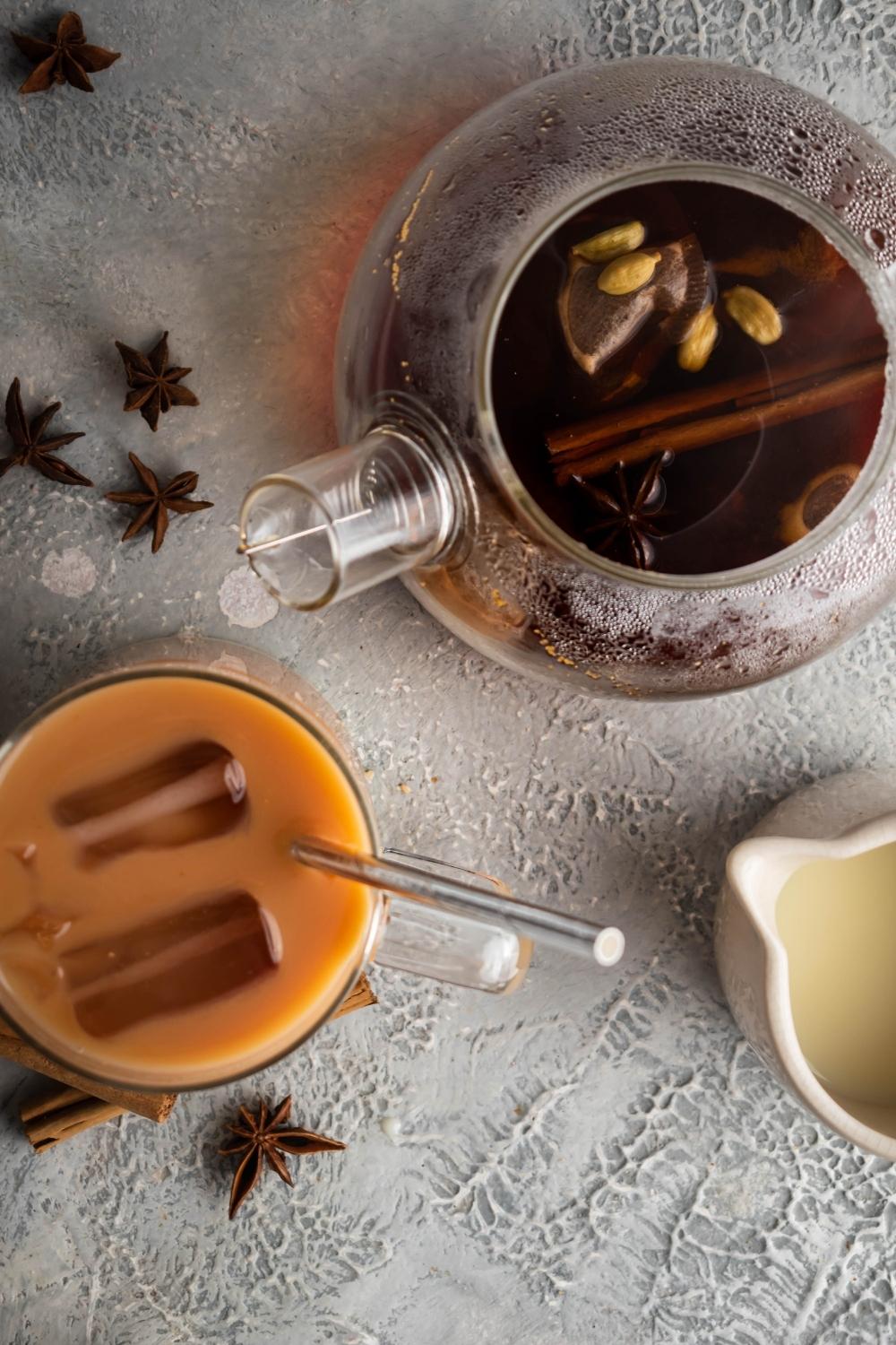 A tea pitched filled with black tea next to a cup filled with thai tea.