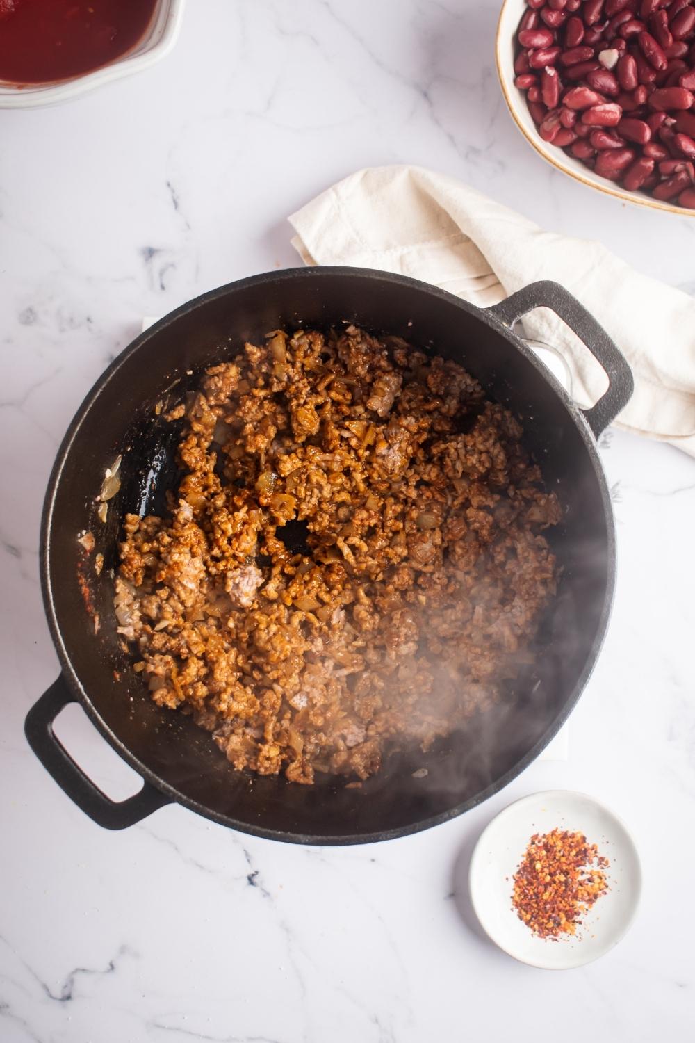 An overhead view of a skillet with cooked ground beef steaming.