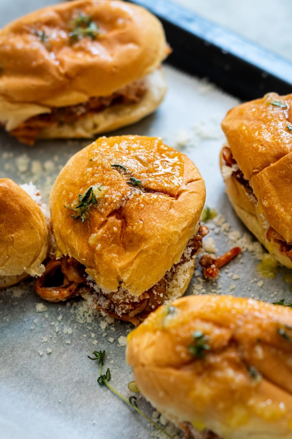 BBQ shredded chicken sliders on a parchment lined baking tray topped with herb-butter ready to be cooked in the oven..