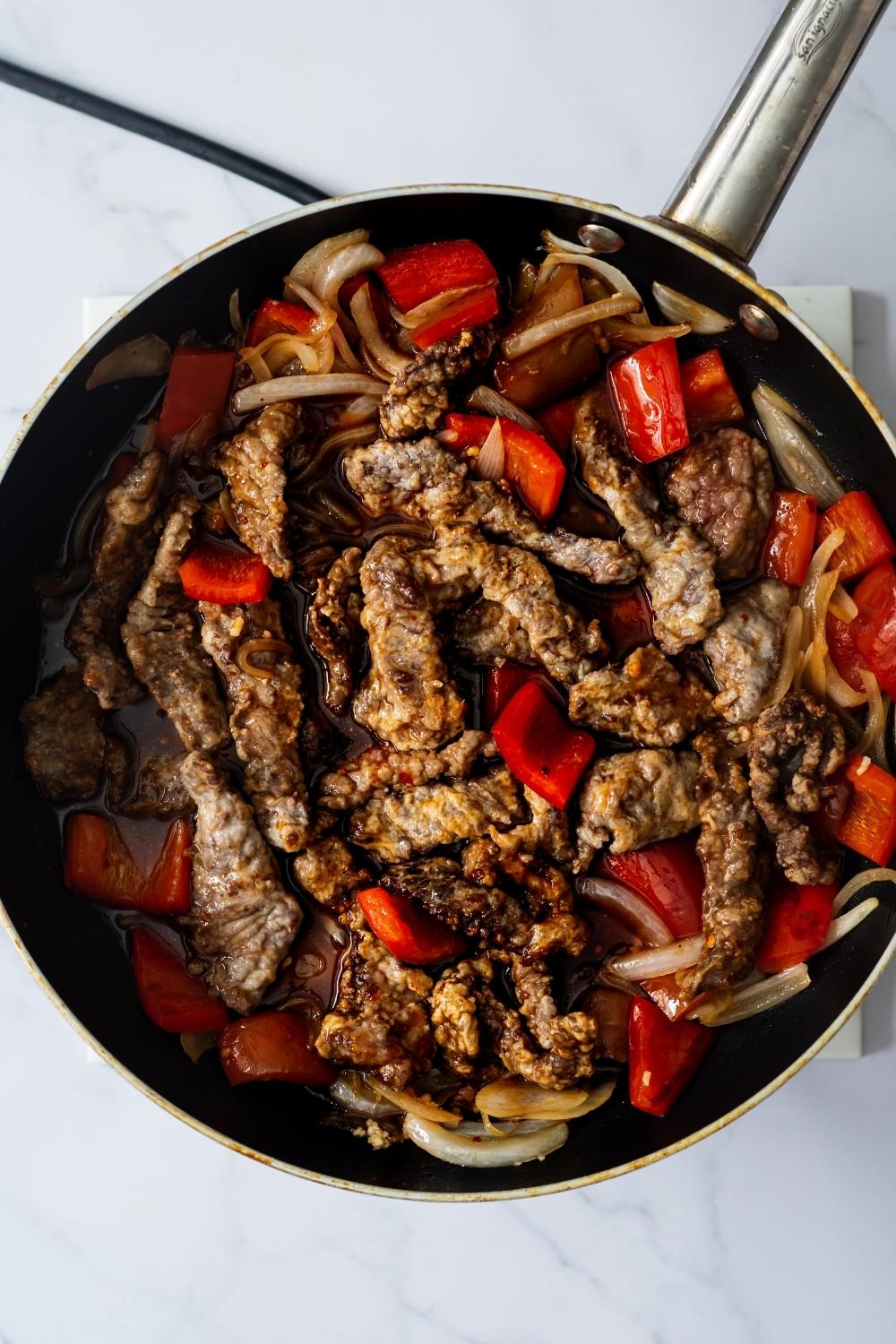 An overhead view of a pan with homemade Beijing beef, peppers, onions being cooked together.