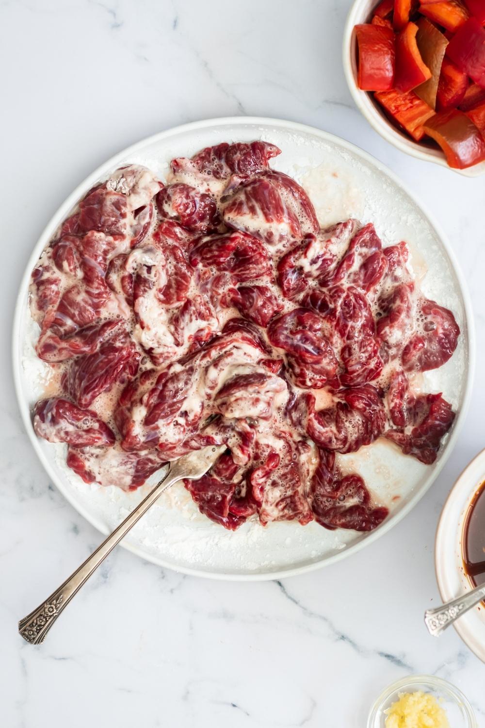 An overhead view of sliced beef that has been mixed with cornstarch, egg white, and salt.