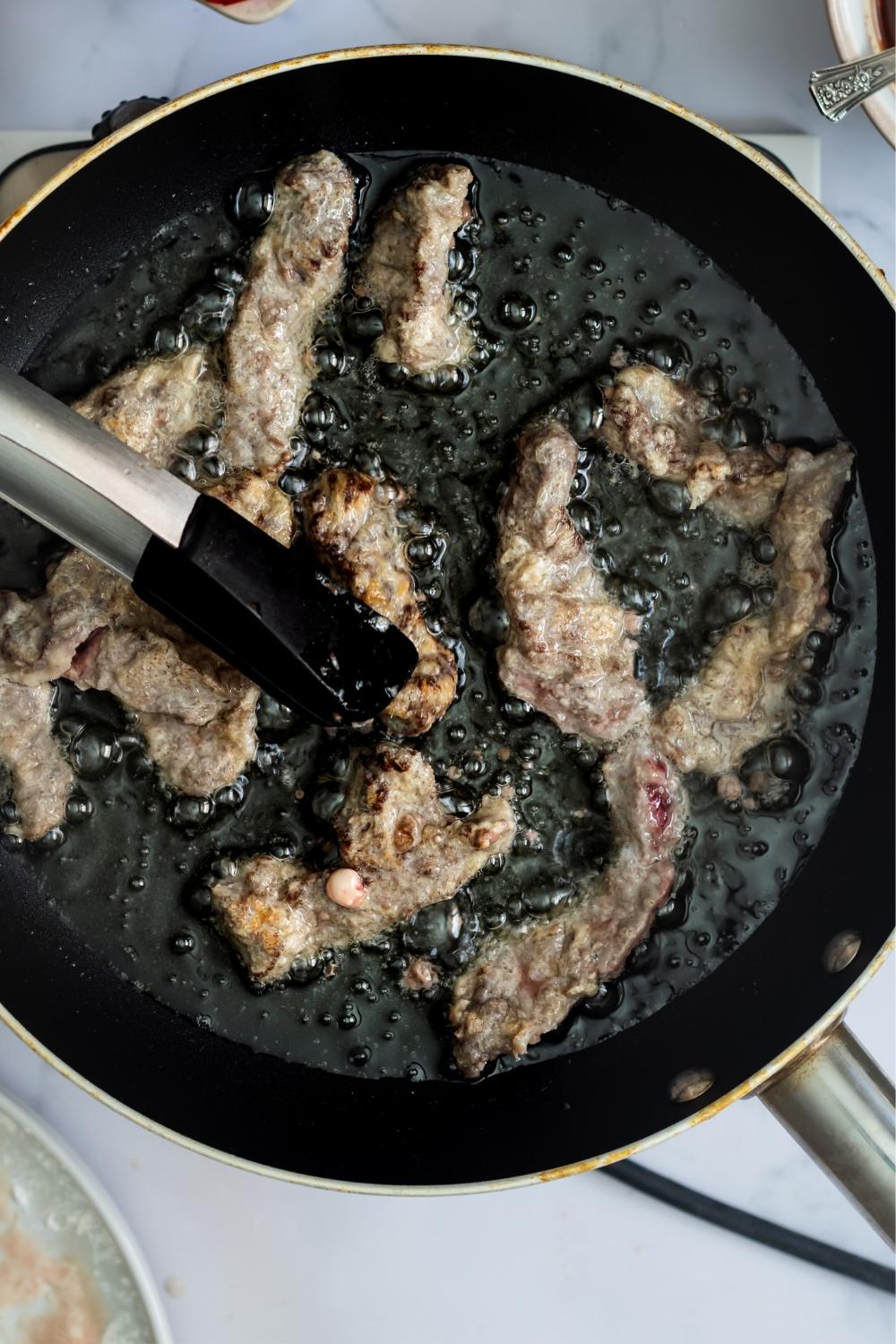 An overhead view of a skillet with hot oil frying sliced beef.