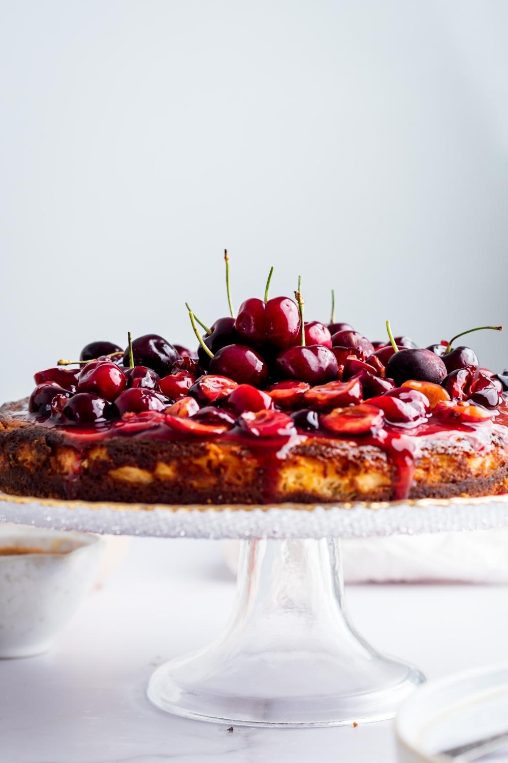 A cherry cheesecake piled high with cherries on a cake stand.