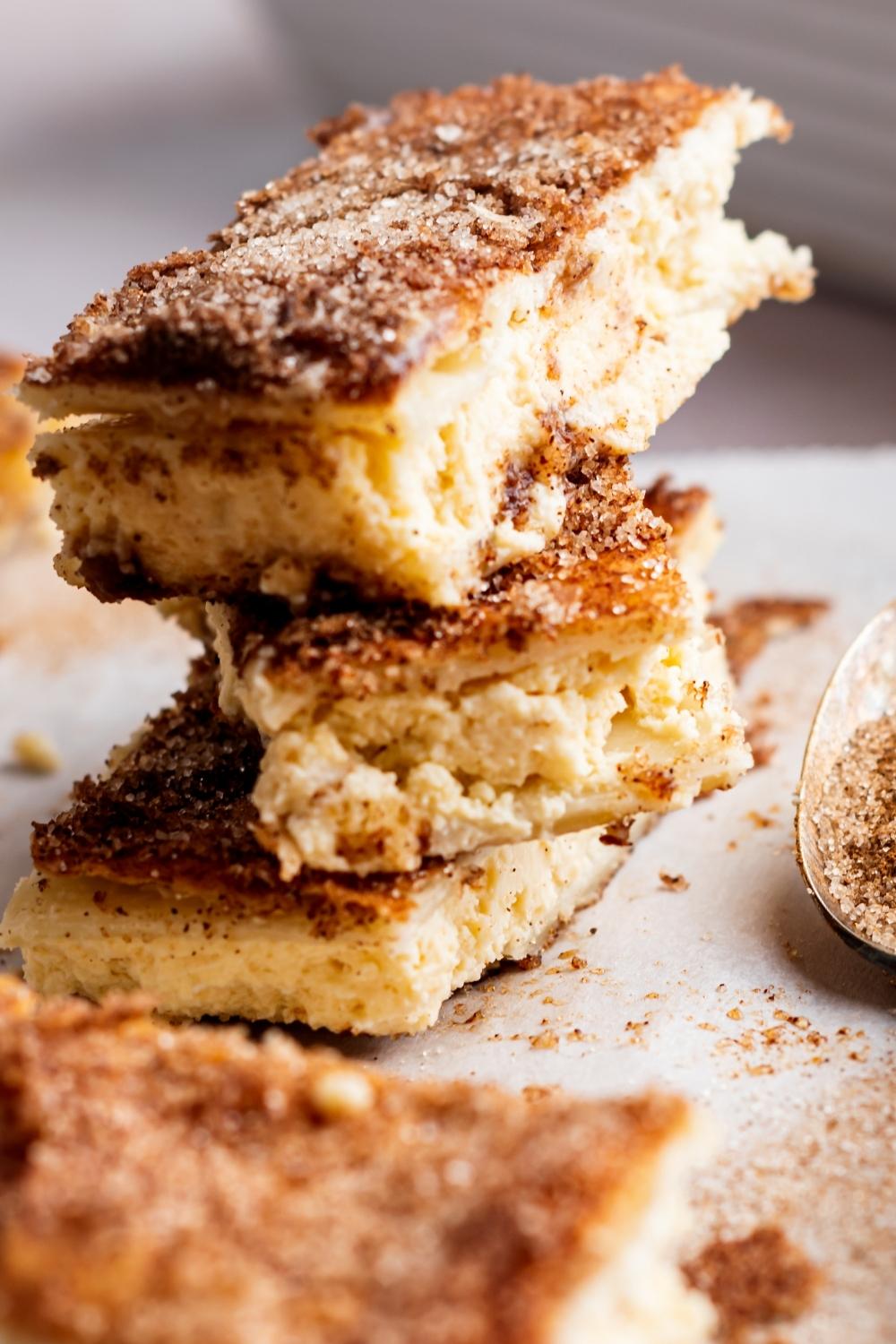 A close-up of a stack of three churro cheesecake bars. Each one is topped with cinnamon and sugar mix.