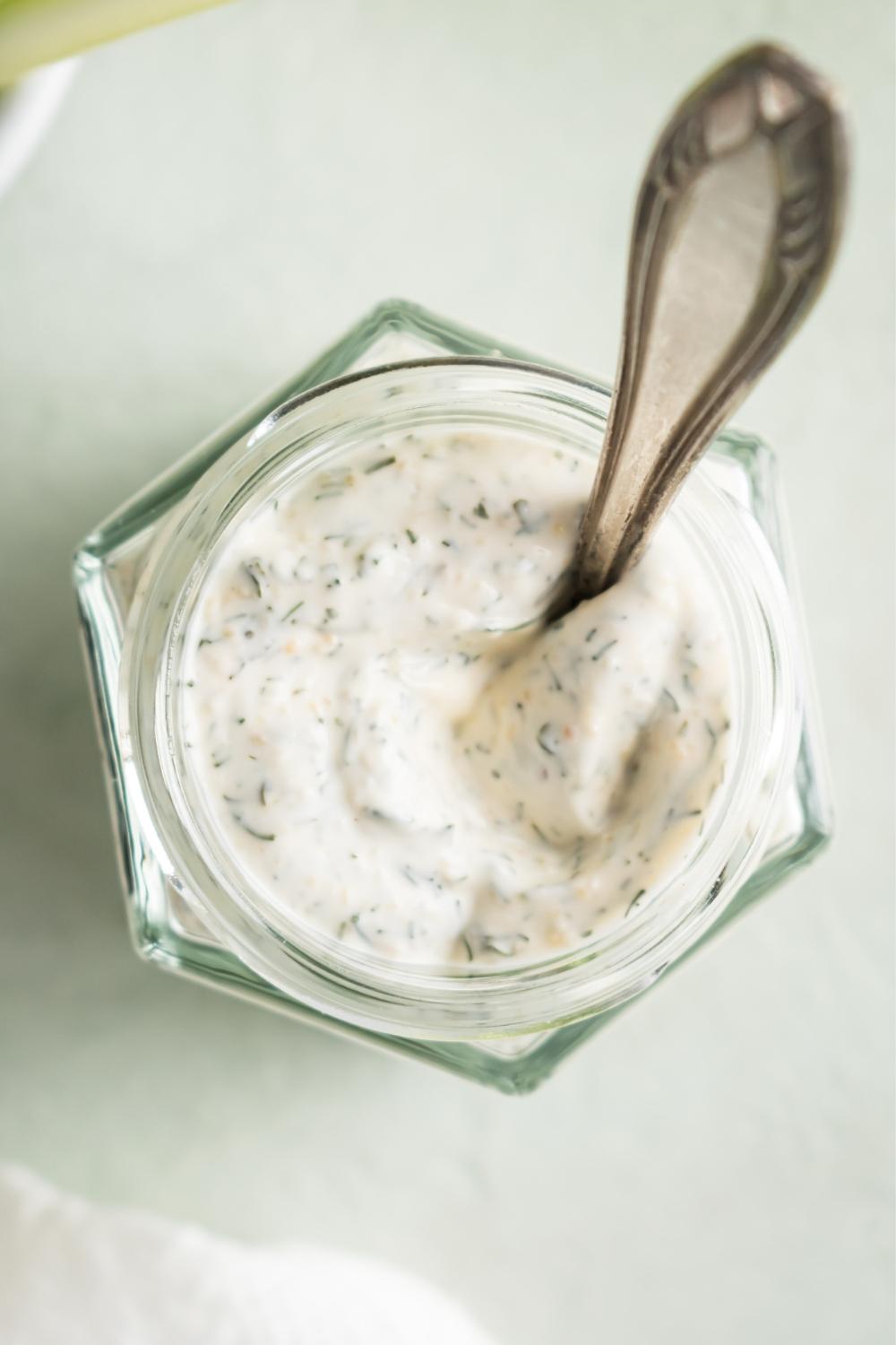 An overhead view of a mason jar containing dill dip in it with a spoon.