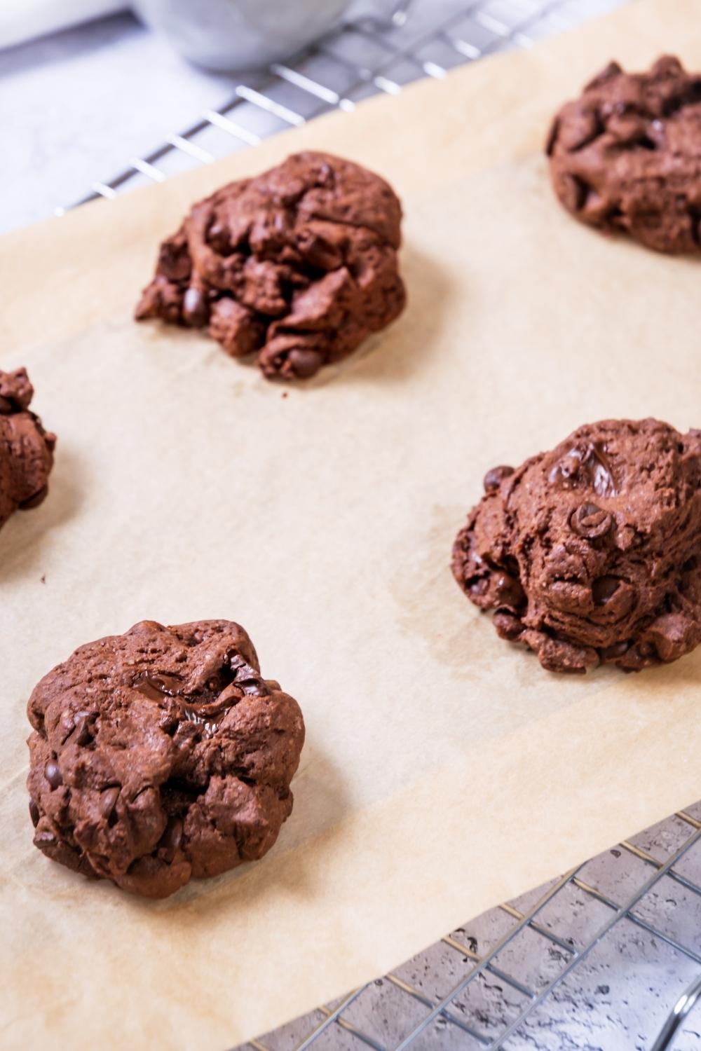 A close-up of a parchment paper lined cooling rack with six double chocolate chip cookies on it.