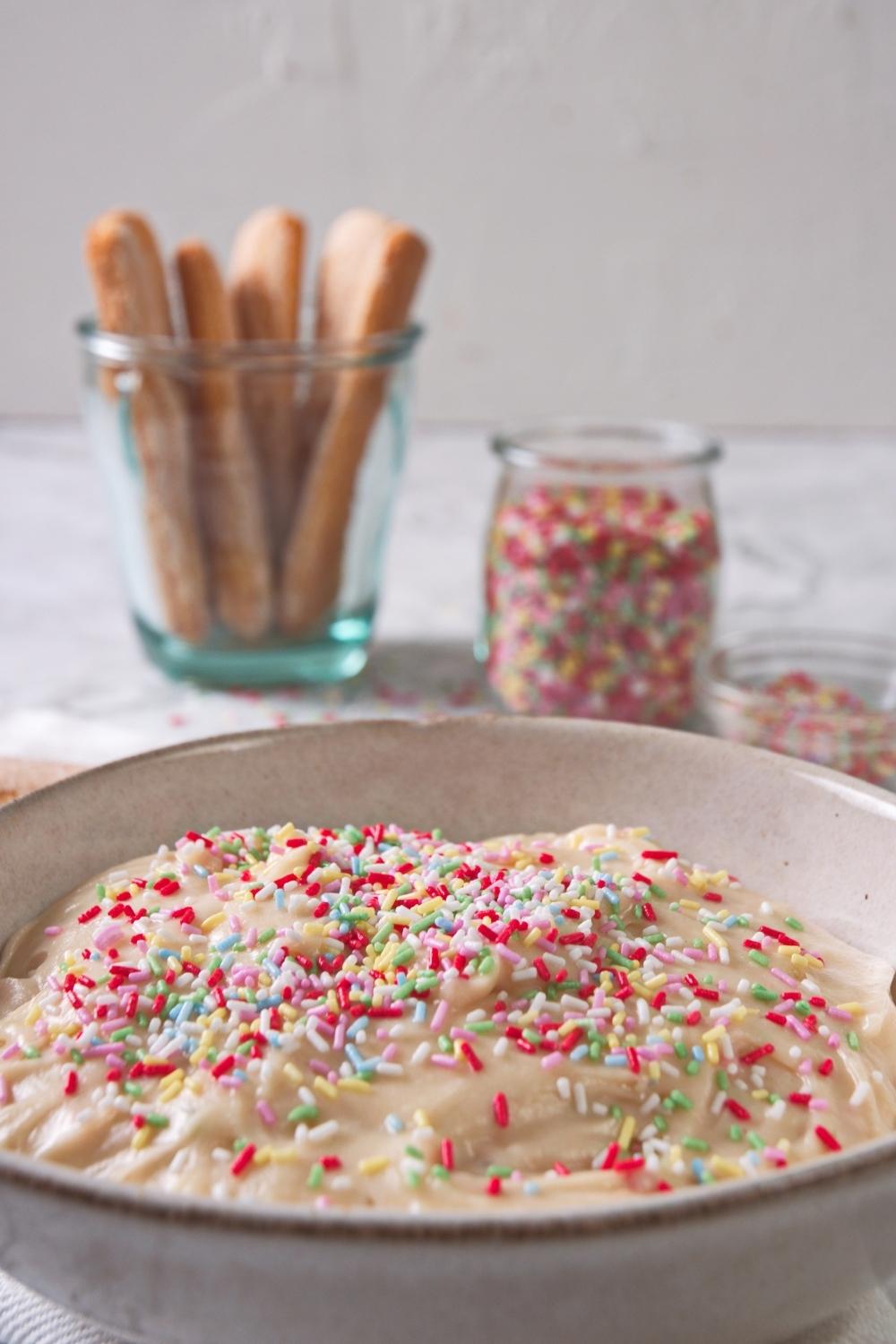 A close-up of a serving bowl containing homemade Dunkaroo dip topped with rainbow sprinkles.