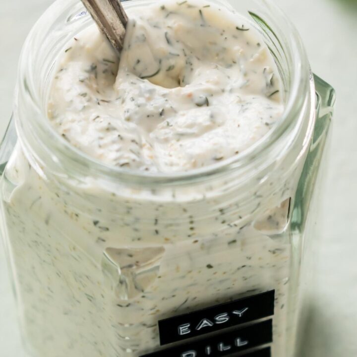 An overhead view of a mason jar containing homemade dill dip with a spoon in it.