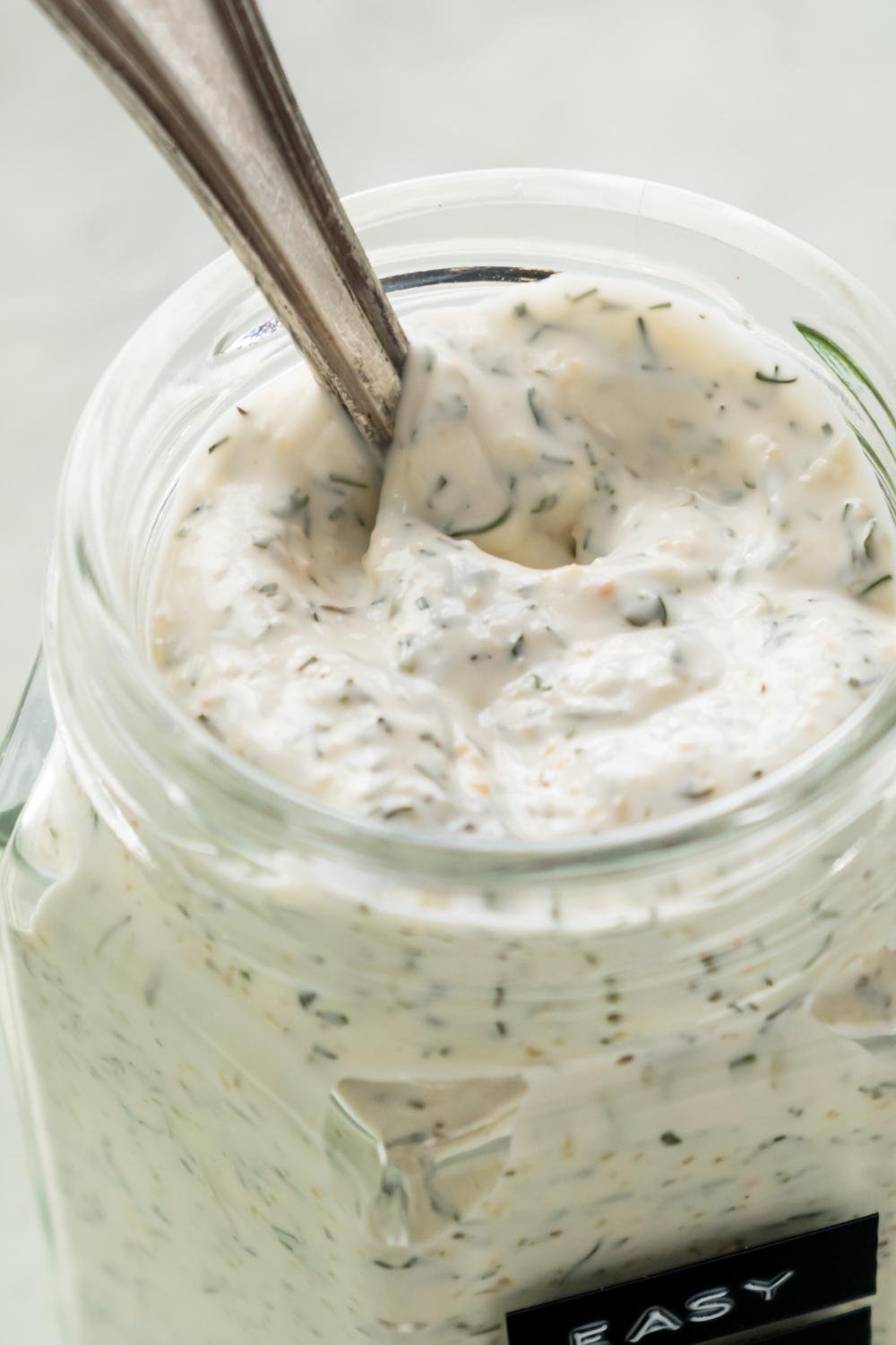 A close-up of a mason jar containing homemade dill dip with a spoon in it.