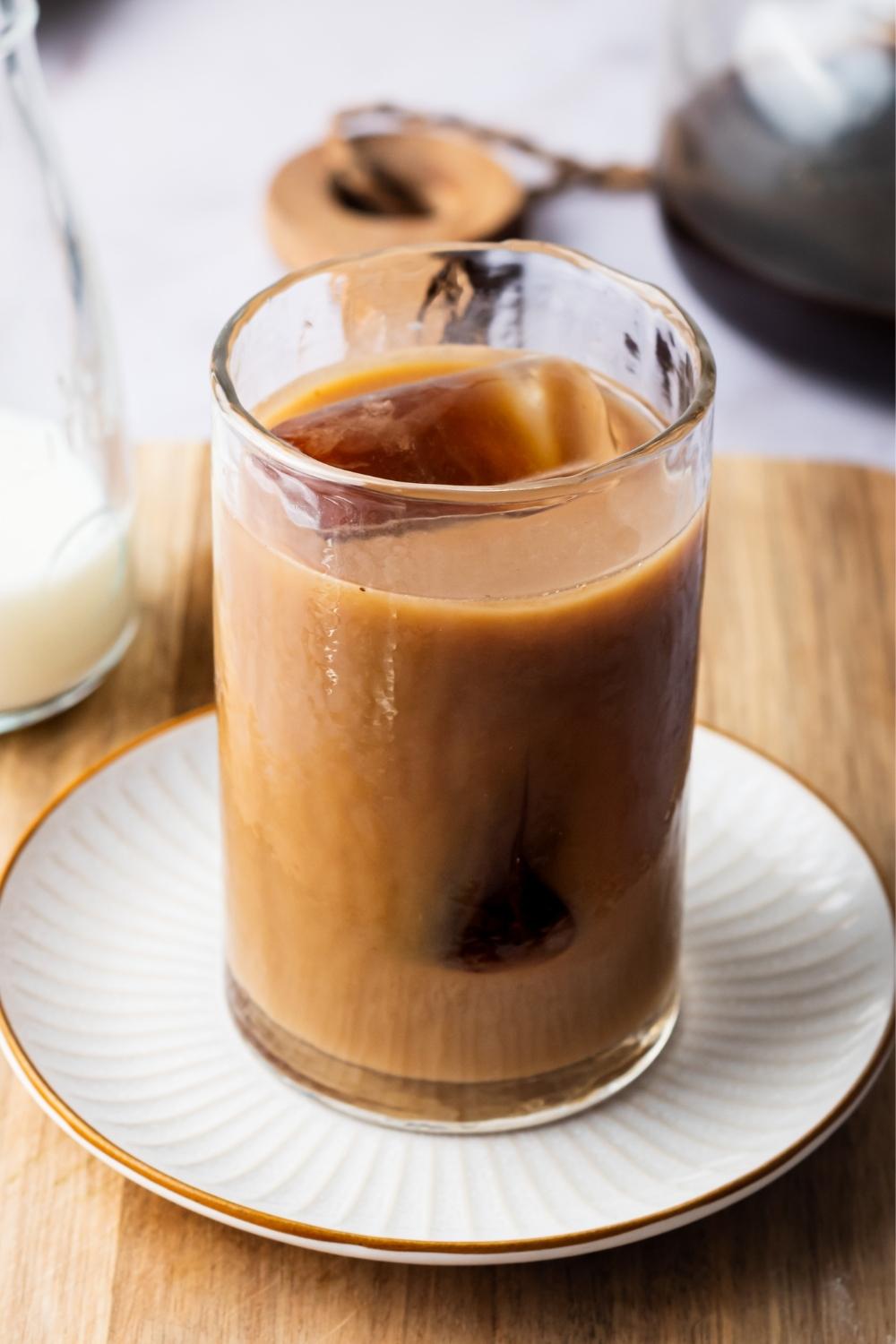 A glass containing iced coffee with cream in it sitting on a saucer.