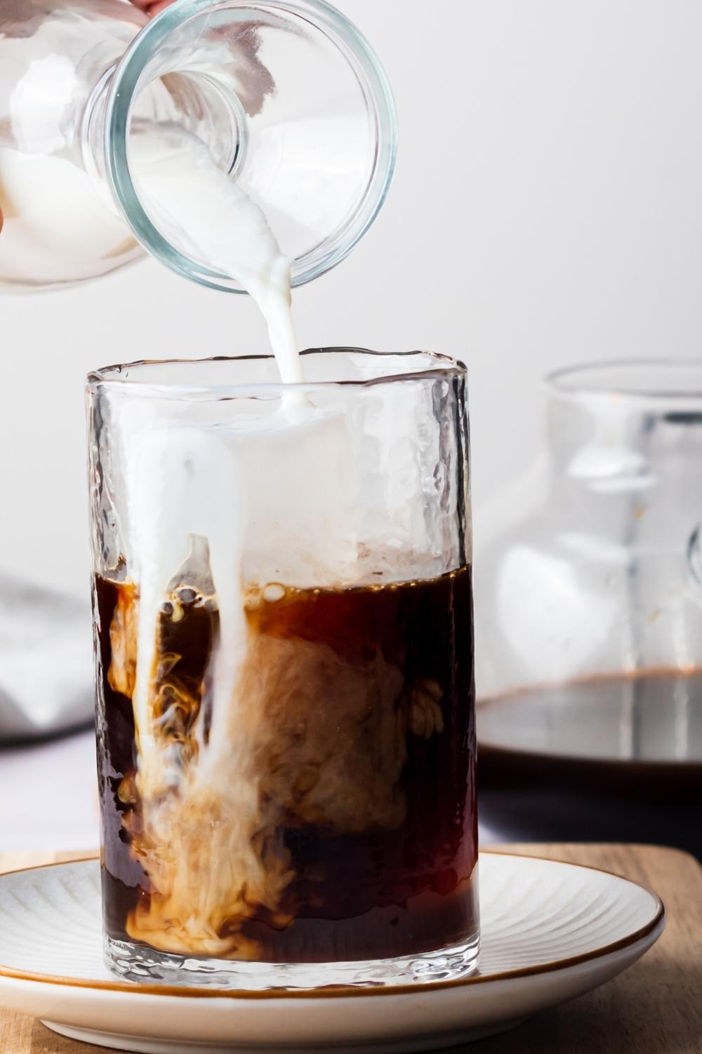 A glass containing homemade McDonald's iced coffee, a pitcher of half and half is being poured into it.