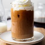 A side view of homemade McDonald's iced coffee topped with whipped cream in a glass.