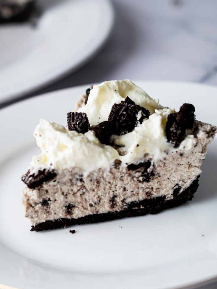 A side view of a slice of homemade oreo pie on a serving plate topped with whipped cream and oreo pieces.