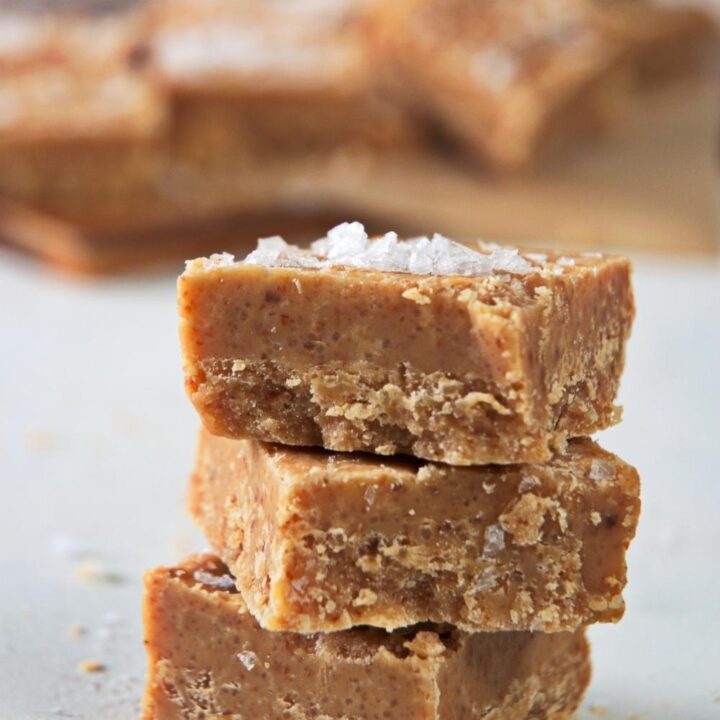 A stack of three caramel fudge squares. Salted caramel is garnished on top.